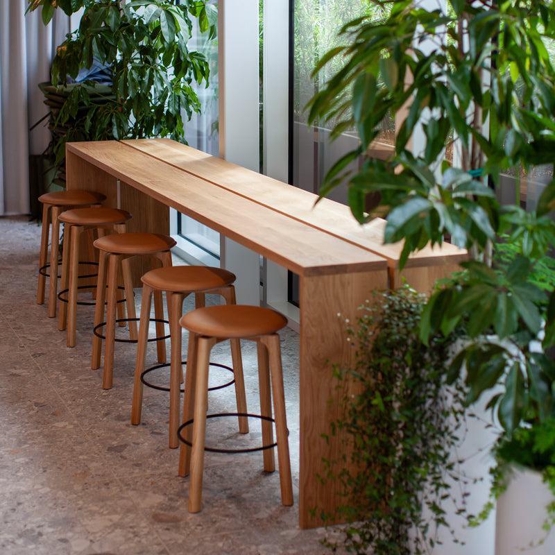 Long wooden table with stools in a modern indoor setting with plants.